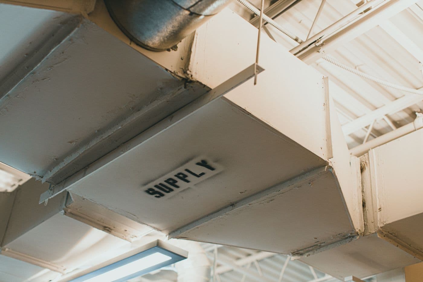 Rectangular sheet-metal supply ductwork running below a ceiling, with a round take-off branch and a register stencilled SUPPLY.