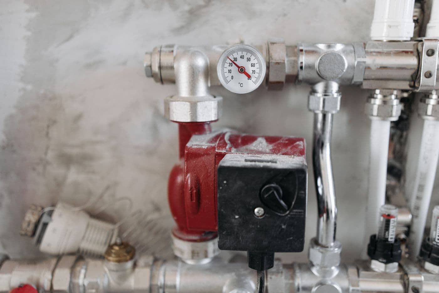 A red circulator pump, a pressure gauge reading mid-scale and a motorised mixing valve on the chrome pipework of a heating system.